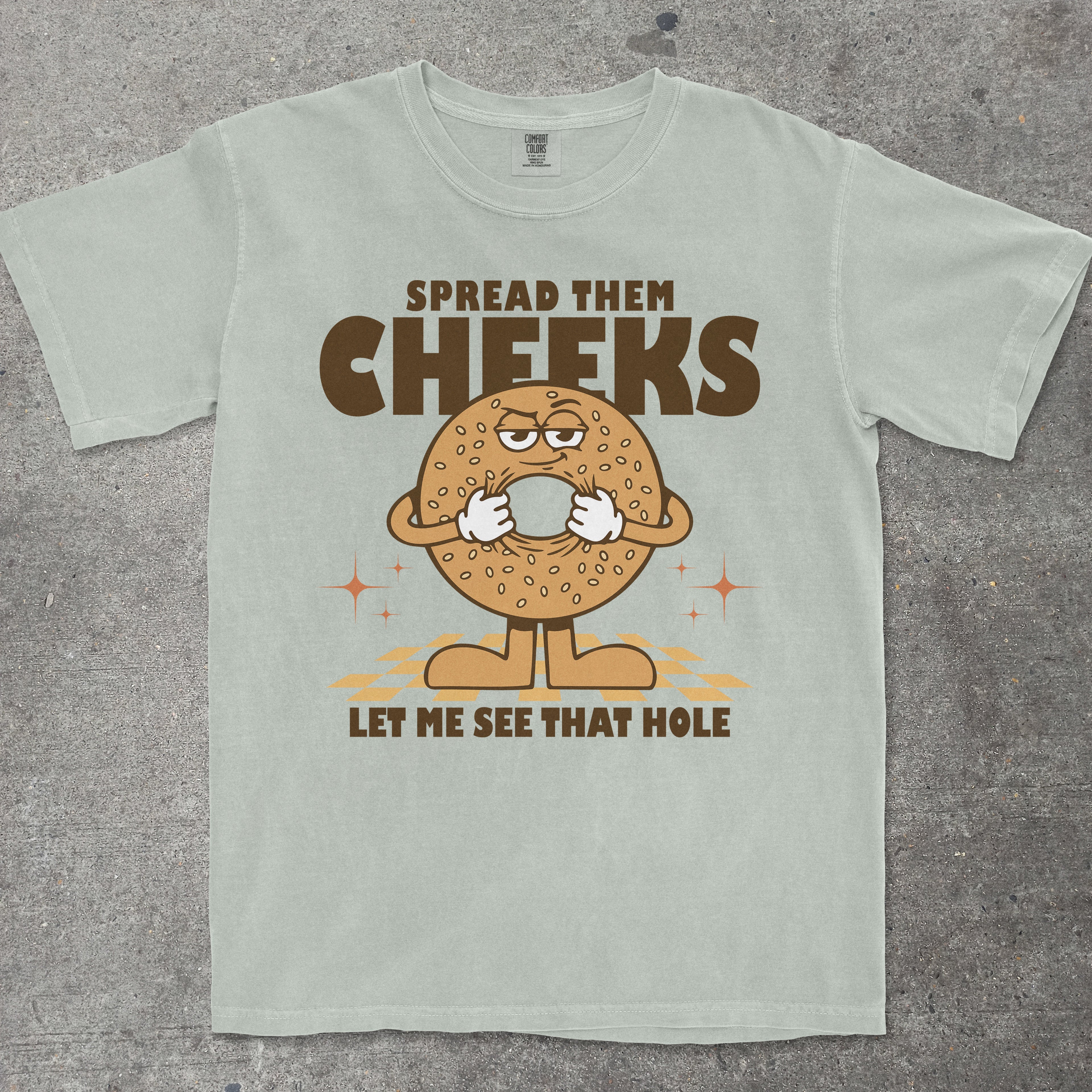 Green t-shirt with a cartoon bagel graphic and humorous text on a gray surface