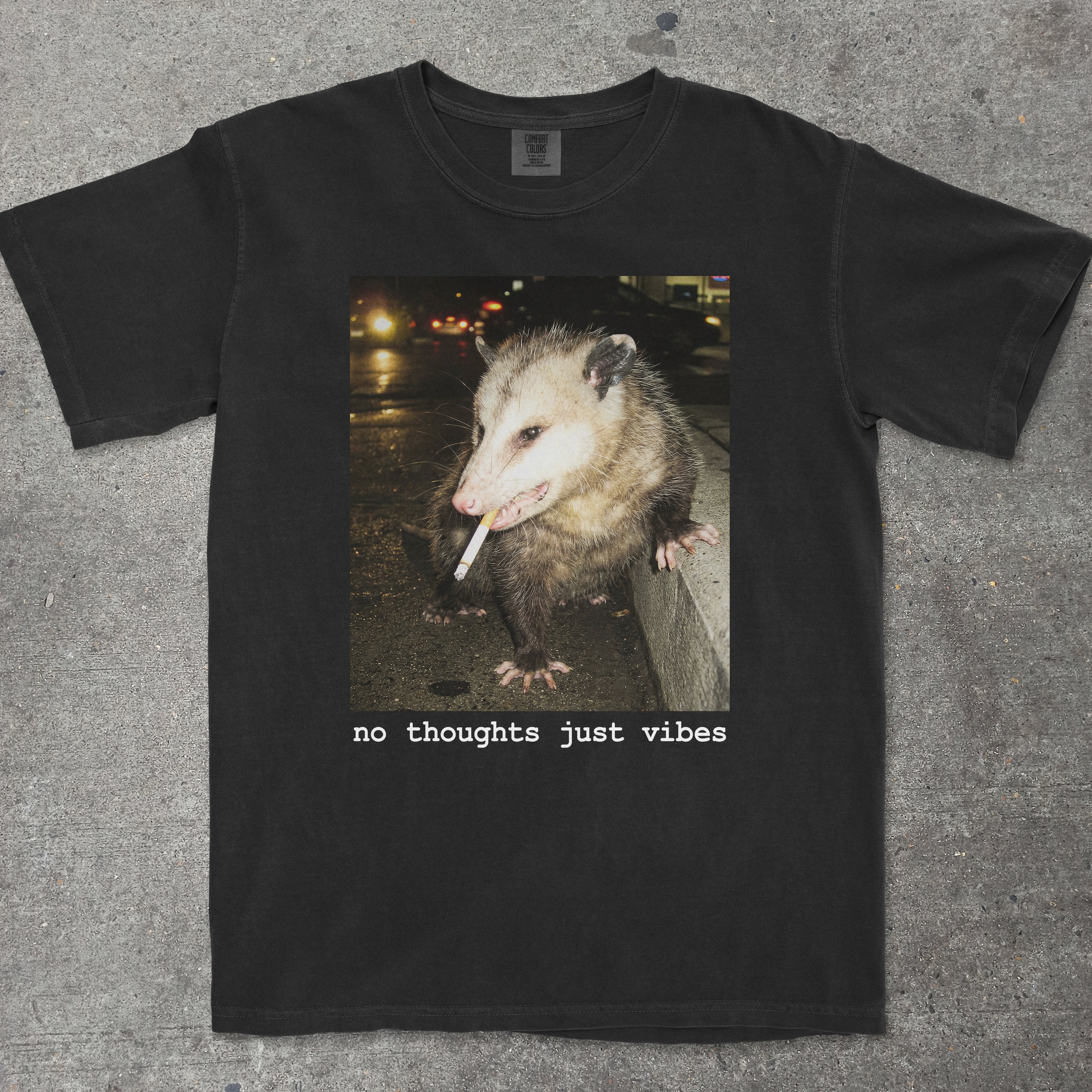 Black t-shirt with an opossum graphic and 'no thoughts just vibes' text on a textured surface.