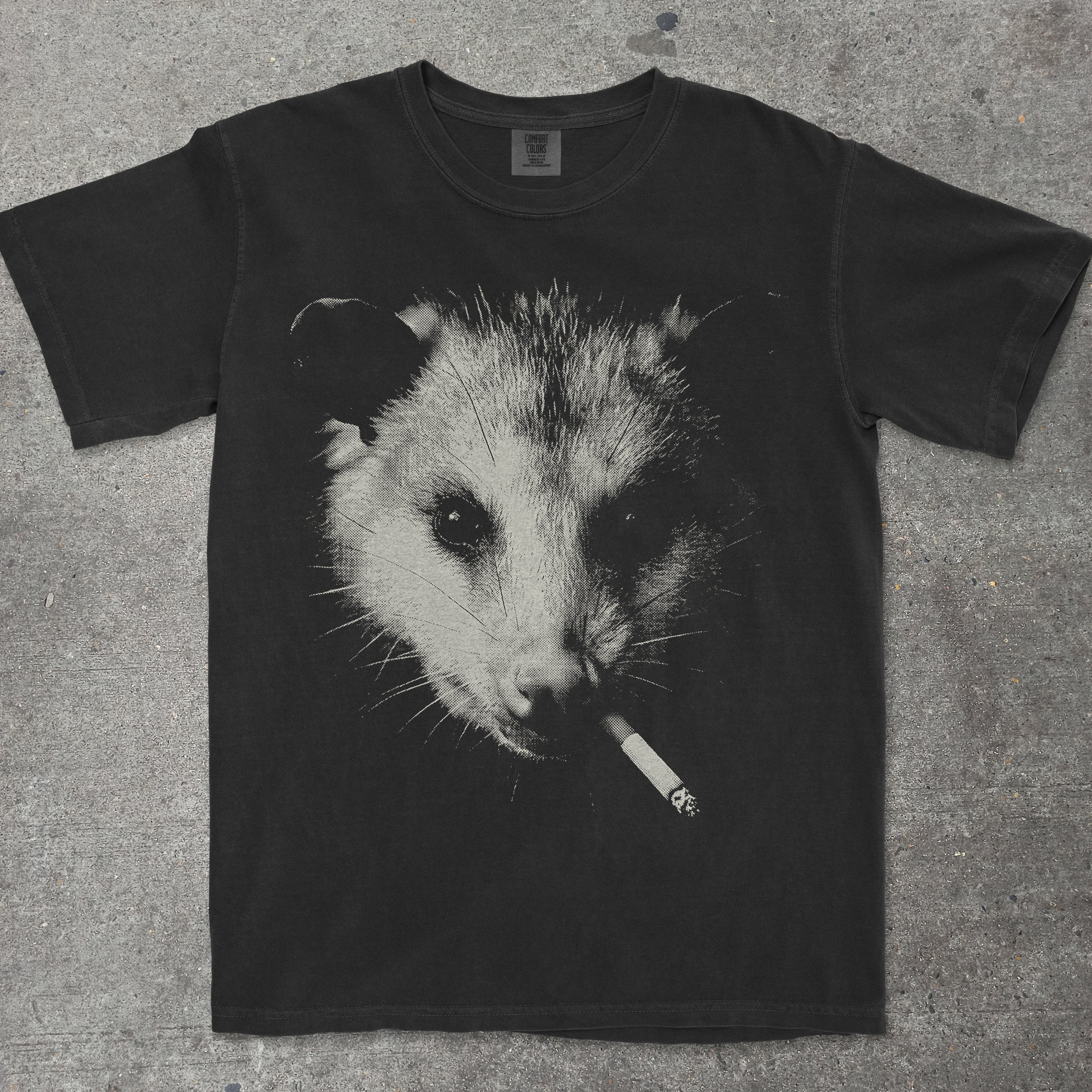 Black t-shirt with an opossum smoking a cigarette graphic on a gray surface