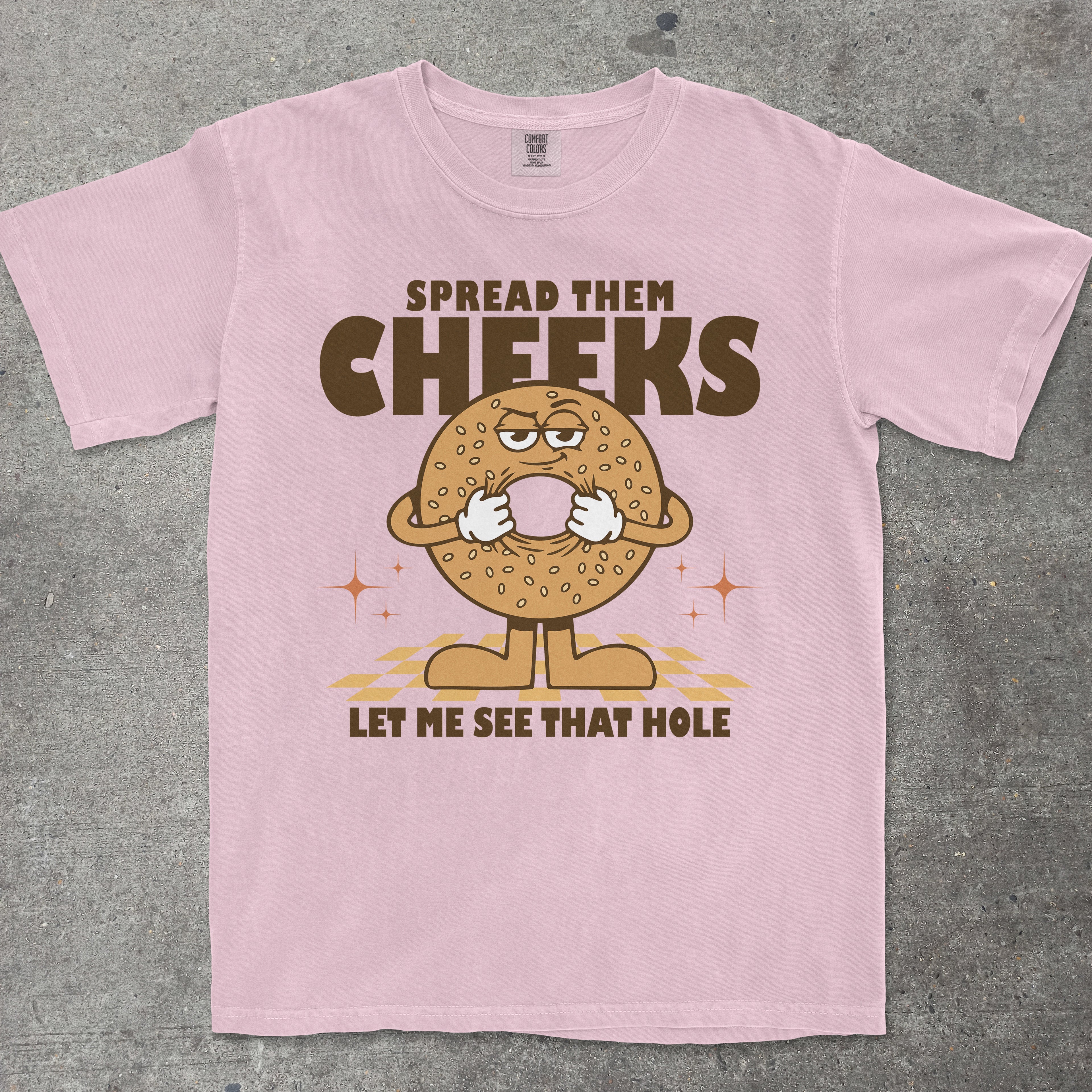 Pink t-shirt with a cartoon bagel character and humorous text on a gray background