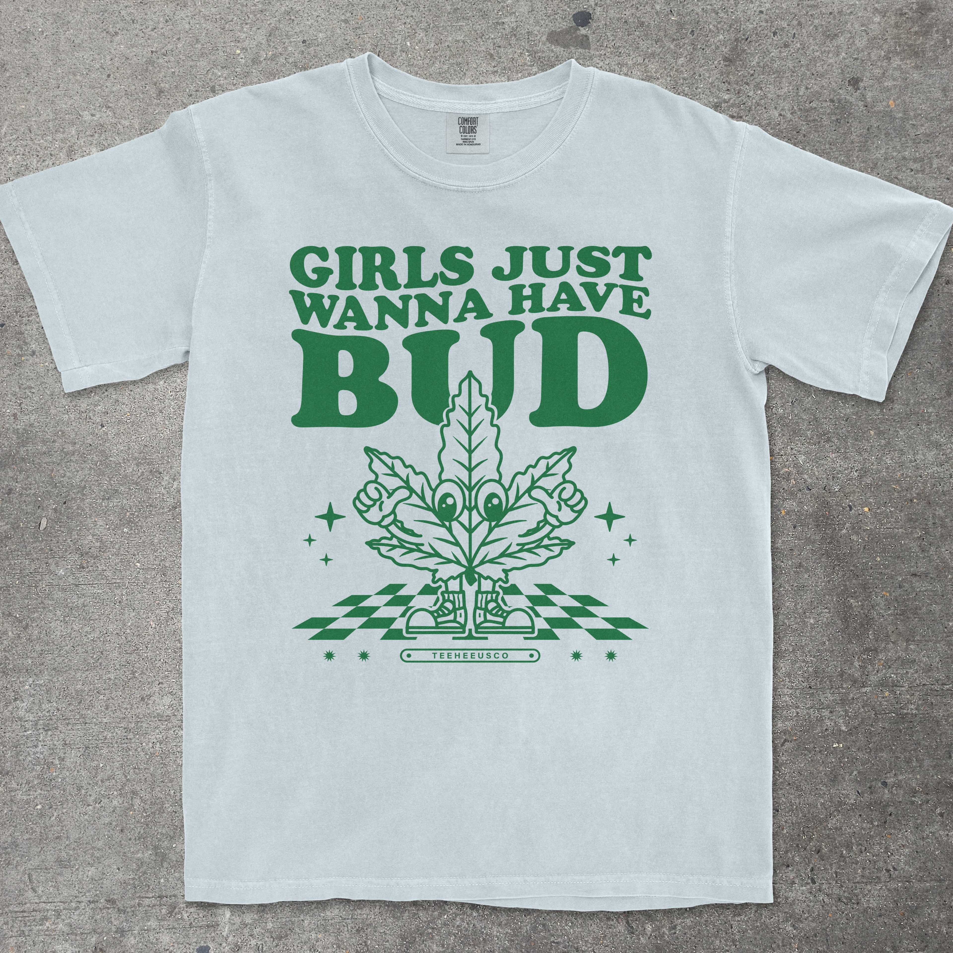 Blue t-shirt with green graphic and text 'Girls Just Wanna Have Bud' on a concrete surface