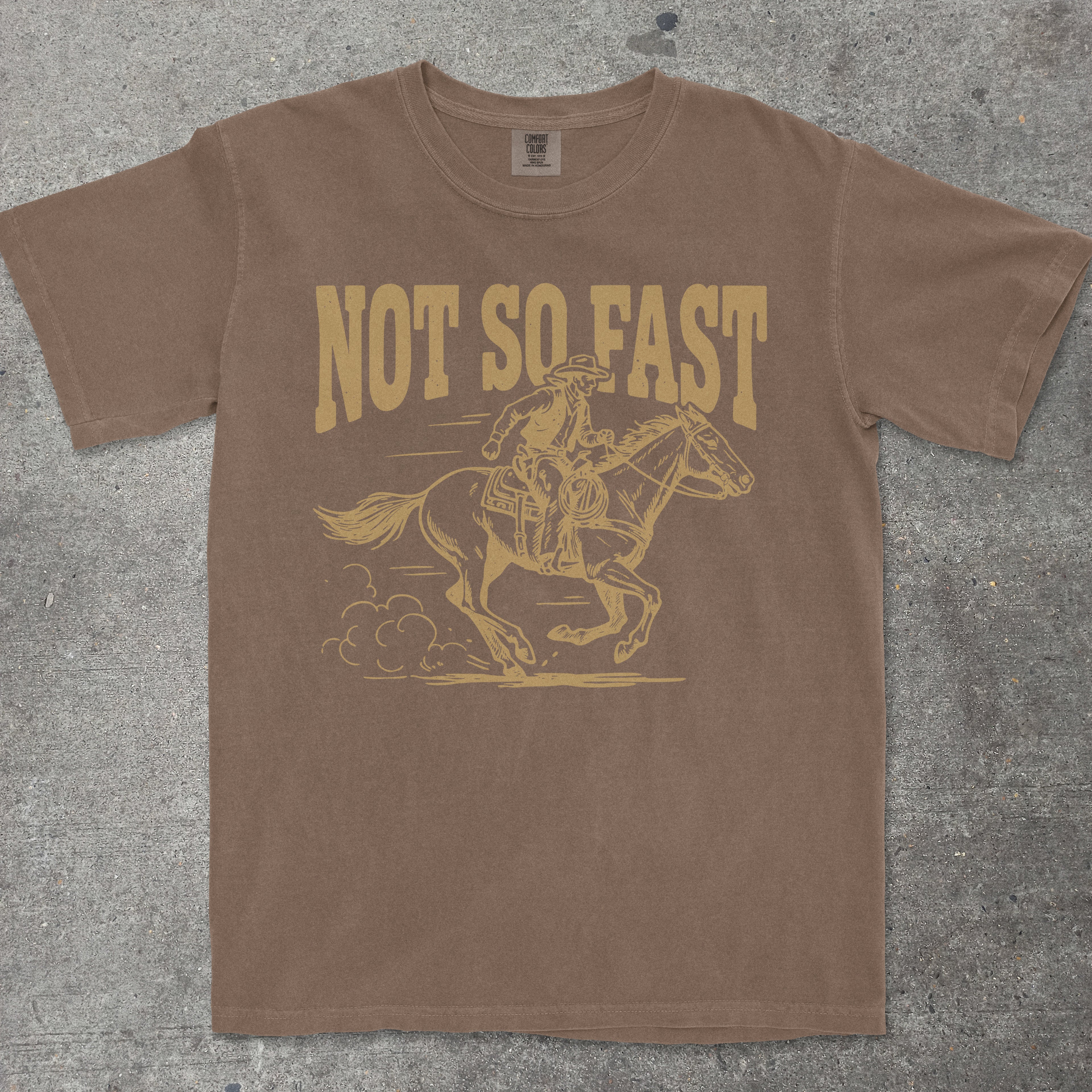 Brown t-shirt with yellow graphic and text 'Not So Fast' on a textured surface