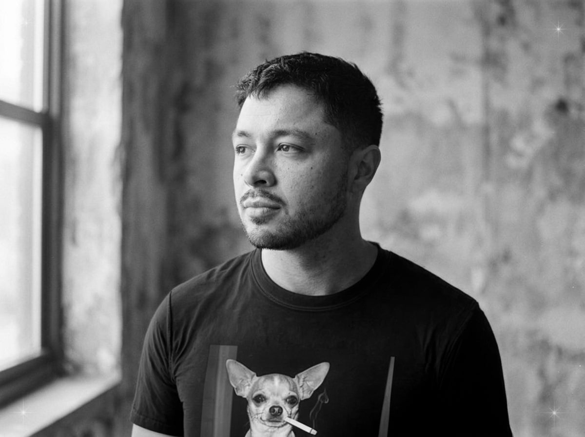 Man wearing a black t-shirt with a dog graphic in a room with a window and textured wall.