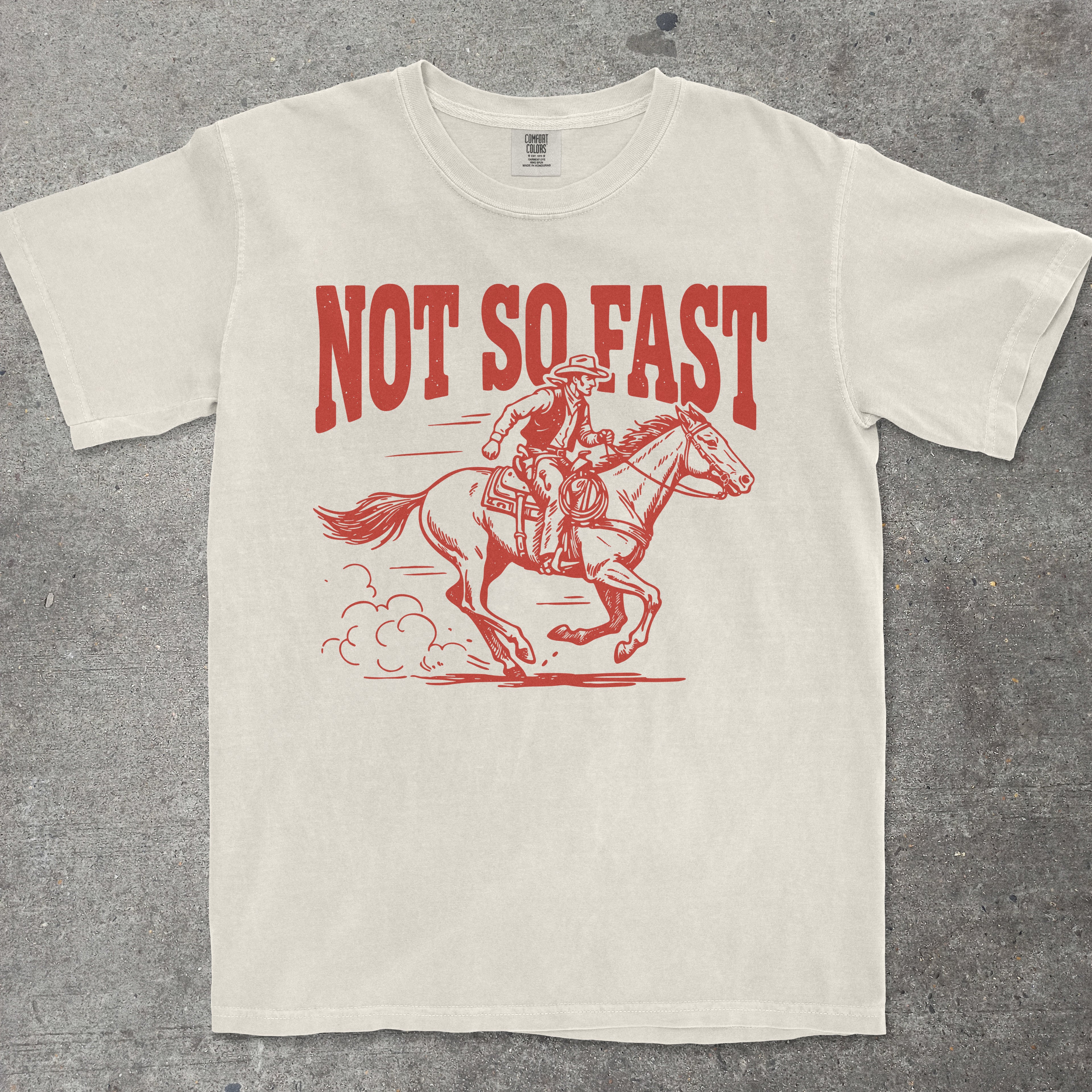 Beige t-shirt with red graphic of a rider on a horse and 'Not So Fast' text on a gray background