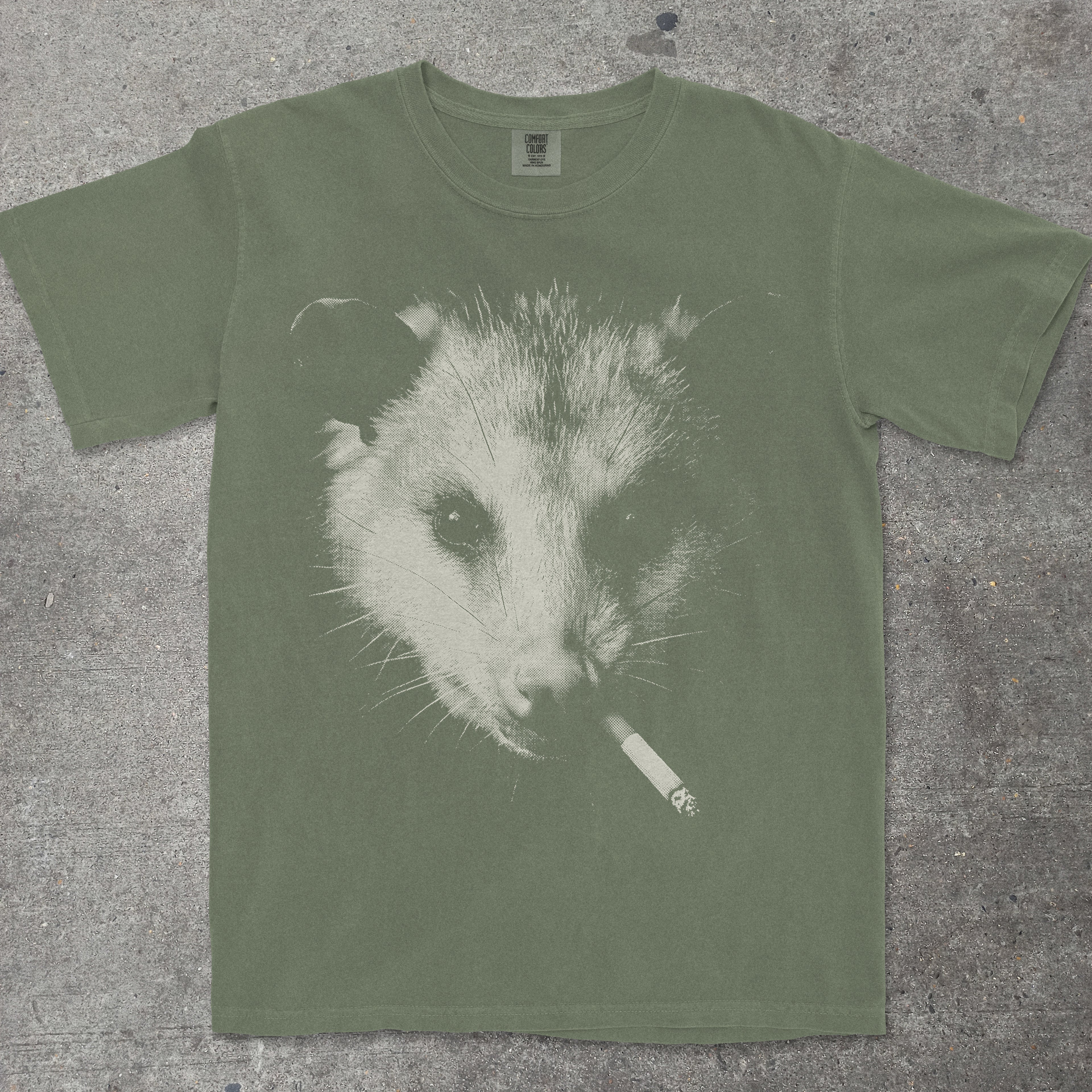 Green t-shirt with an opossum smoking a cigarette graphic on a textured surface
