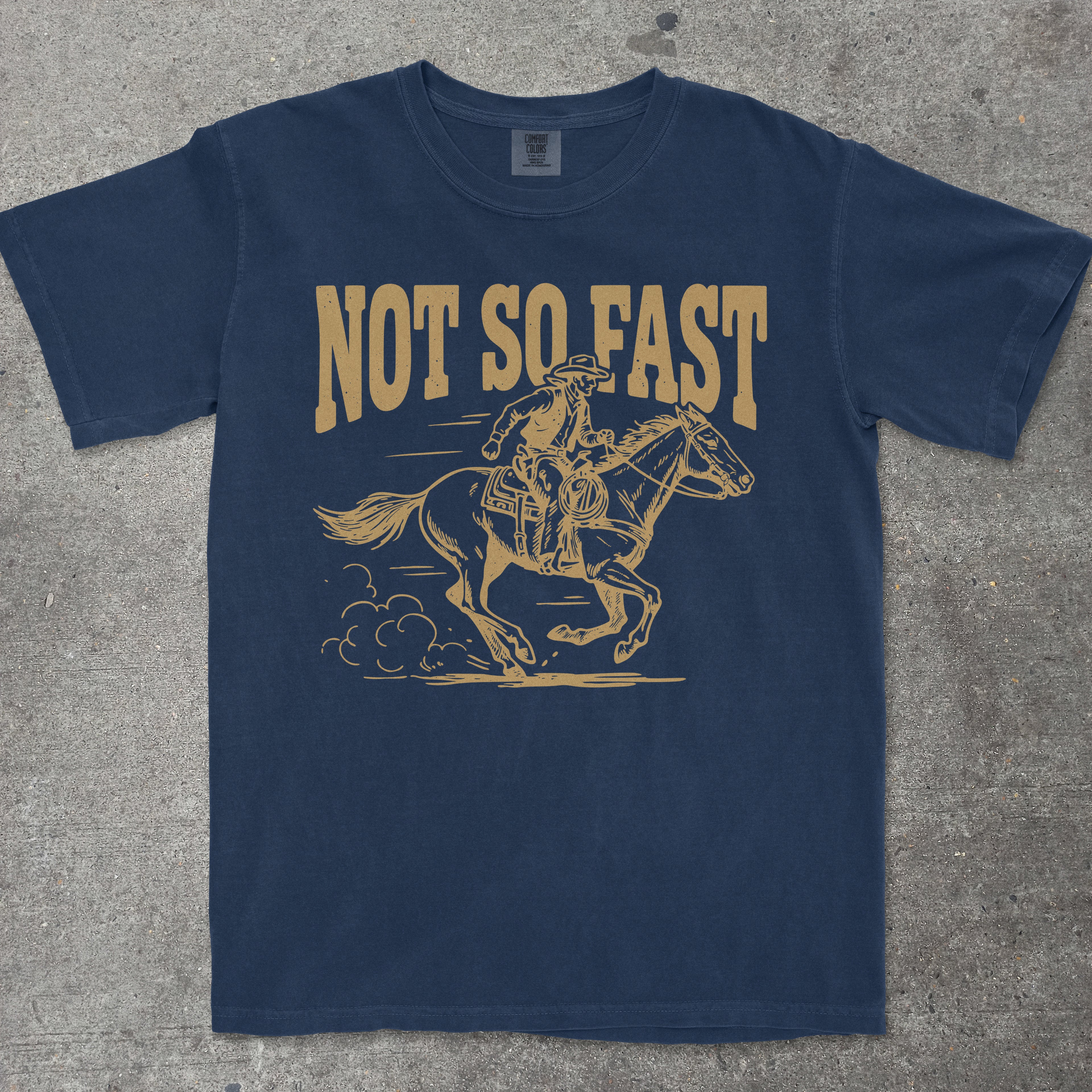 Navy blue t-shirt with yellow graphic of a horse and rider and 'Not So Fast' text on a concrete surface.