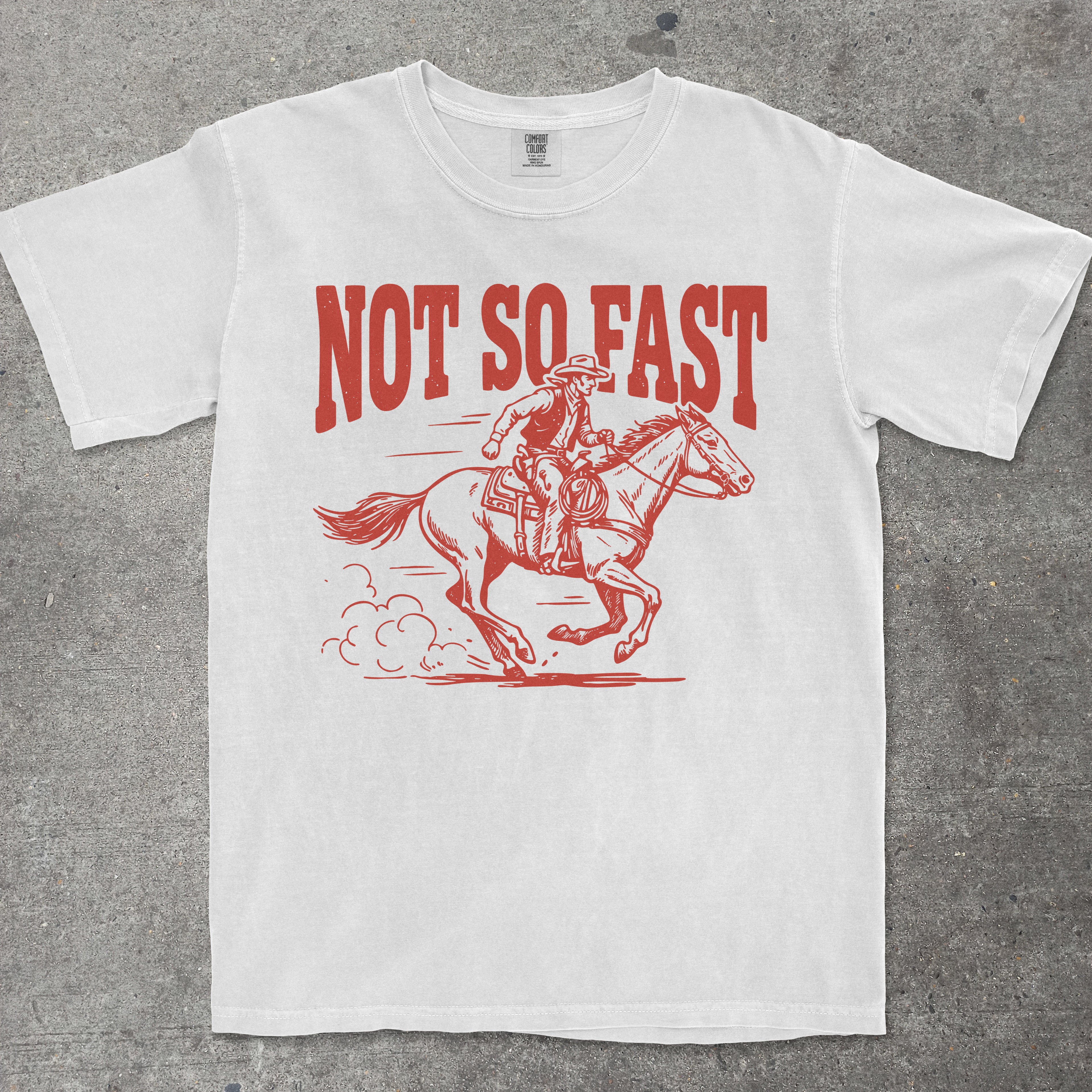 White t-shirt with red graphic of a person on a horse and 'Not So Fast' text on a gray background