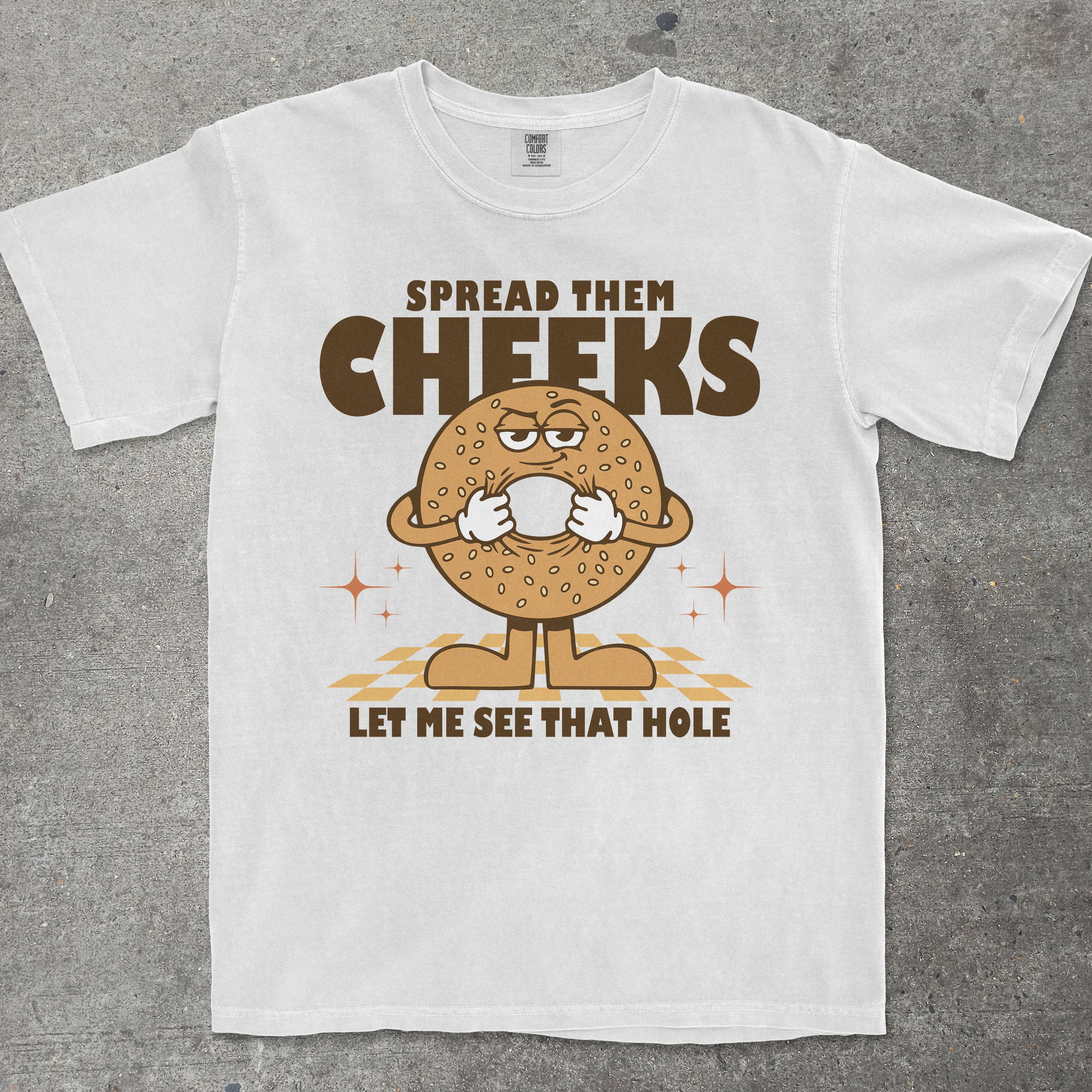 White t-shirt with a cartoon bagel character and humorous text on a gray background