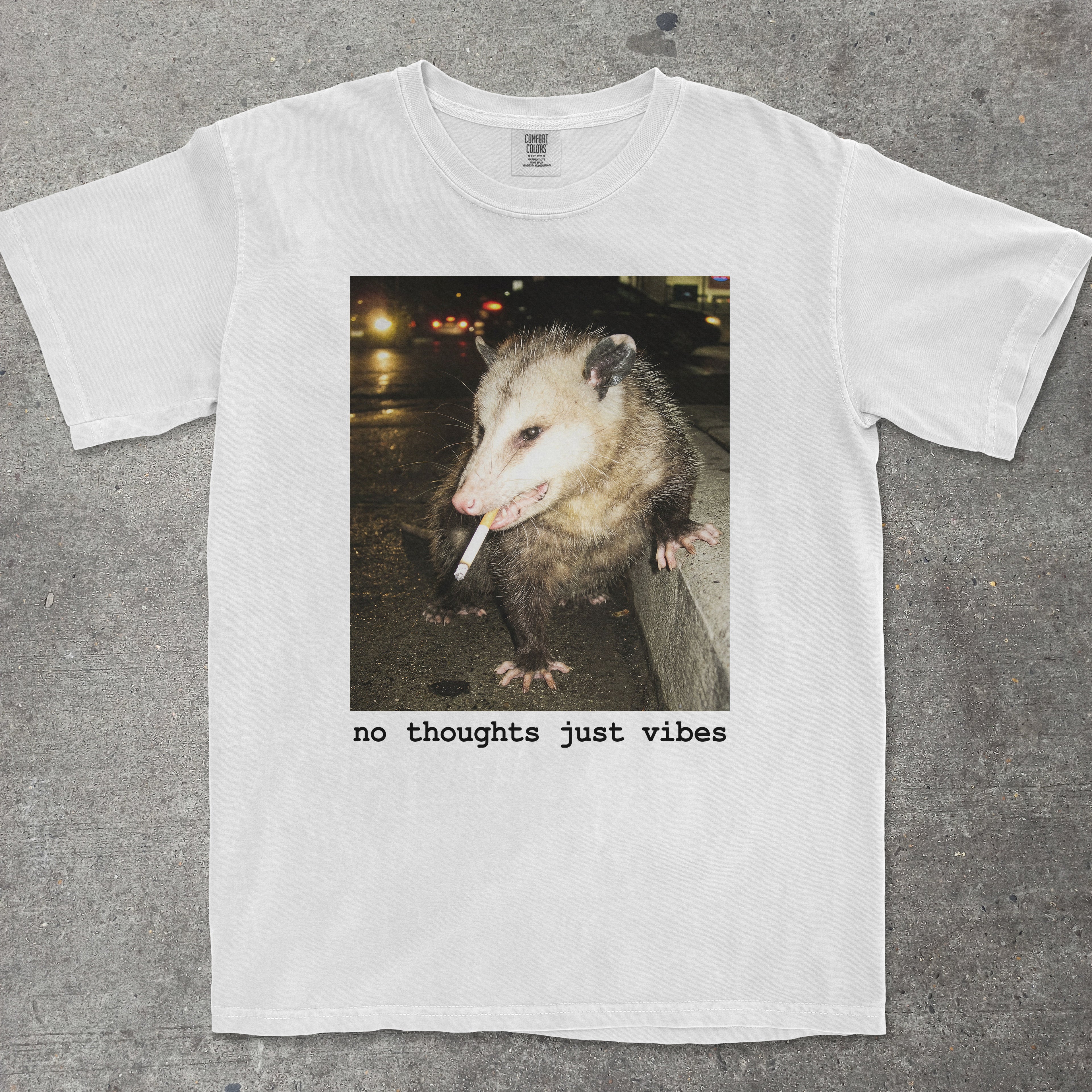 White t-shirt with an opossum graphic and 'no thoughts just vibes' text on a gray background