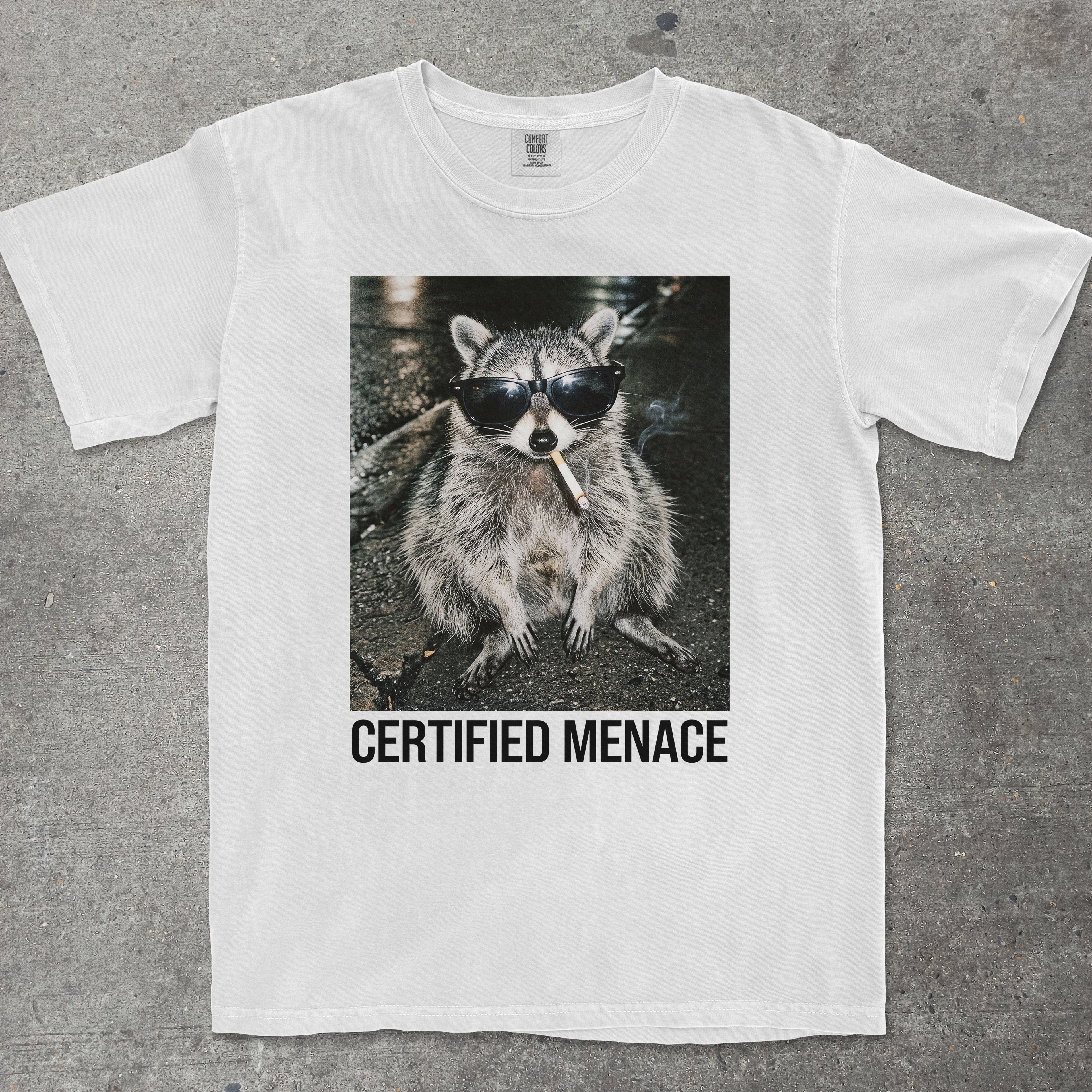 White t-shirt with a raccoon graphic and 'Certified Menace' text on a gray background